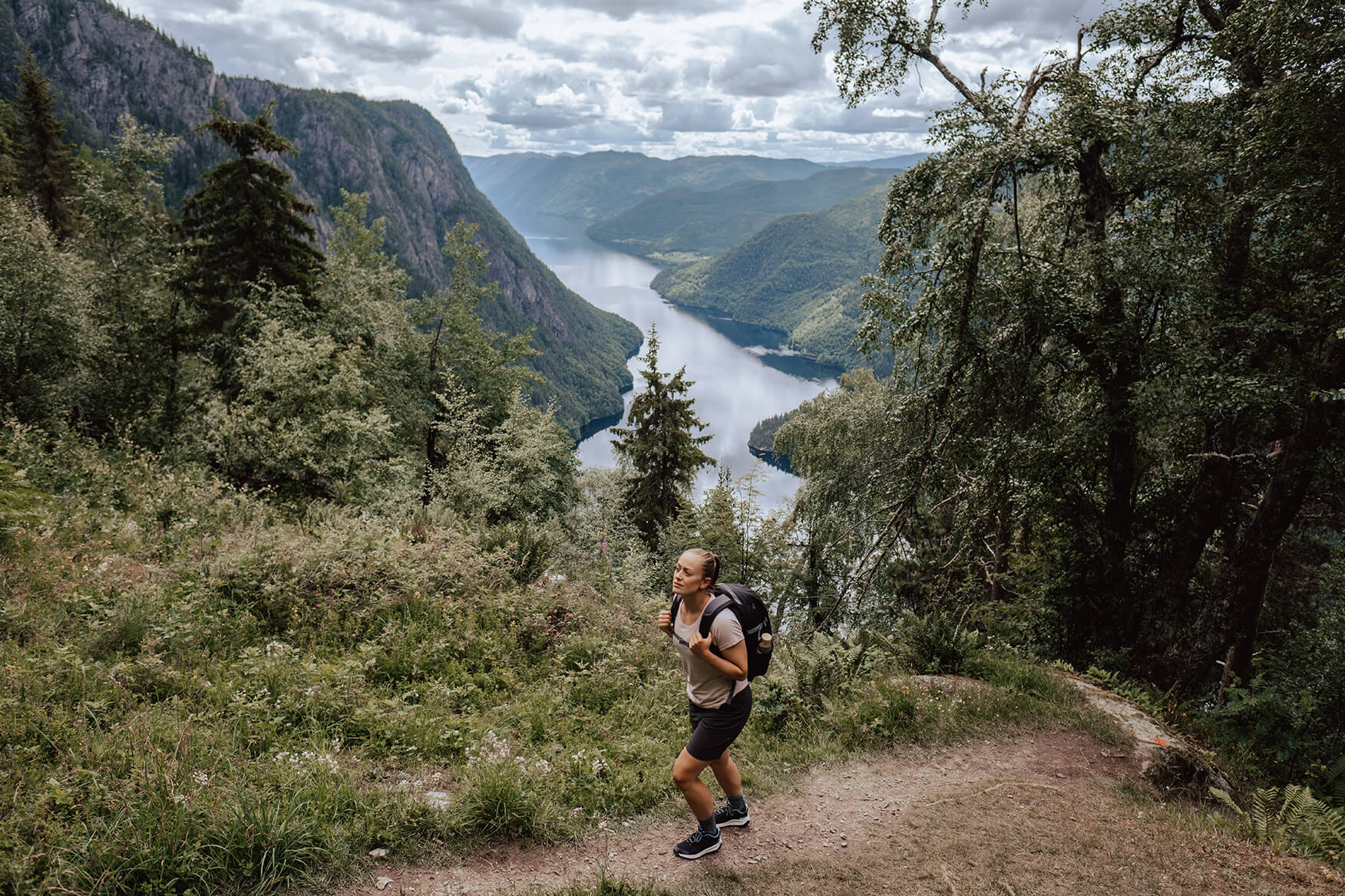 woman hiking on a forest trail above a fjord
