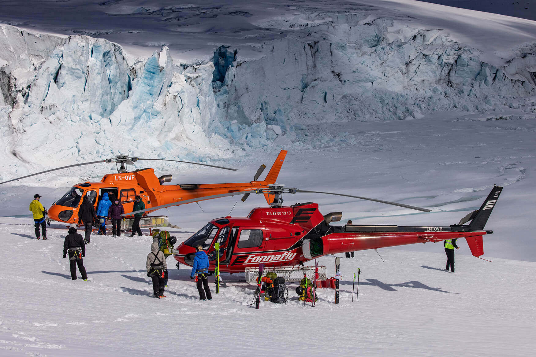 two helicopters with people standing around on a glacier