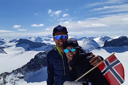 Two people on top of a mountain with a Norwegian flag