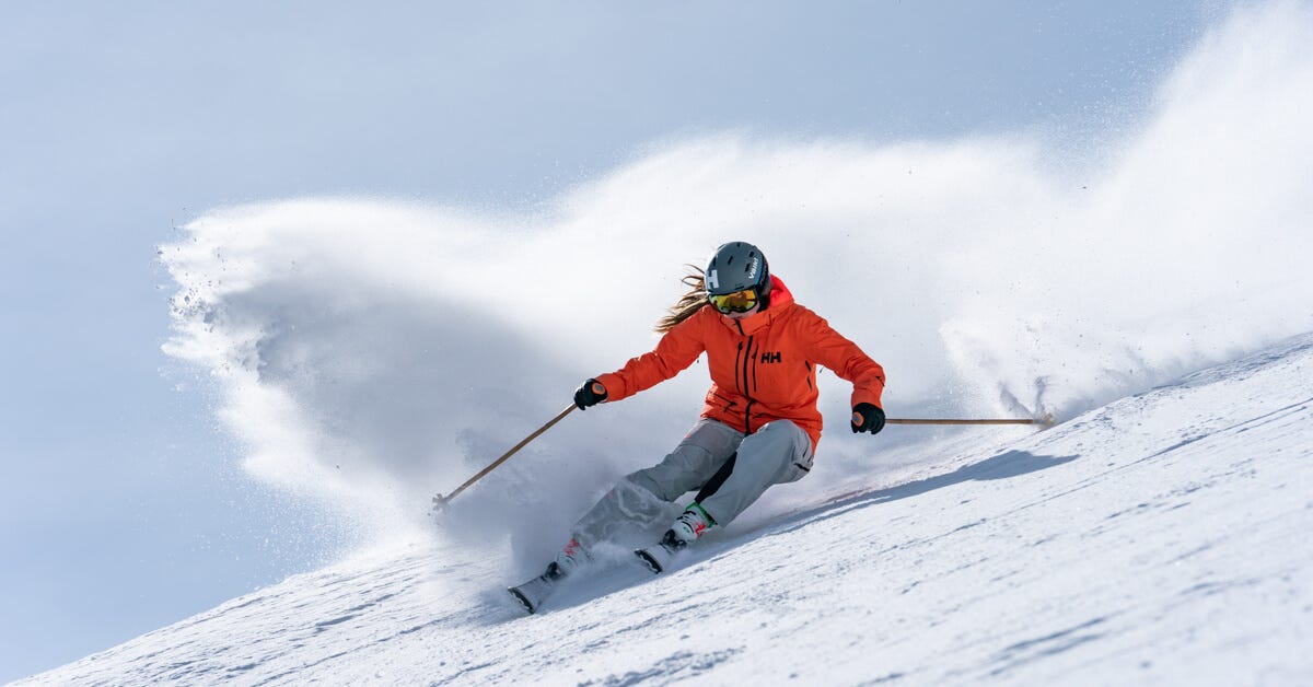 woman skiing down a ski slope in orange helly hansen jacket