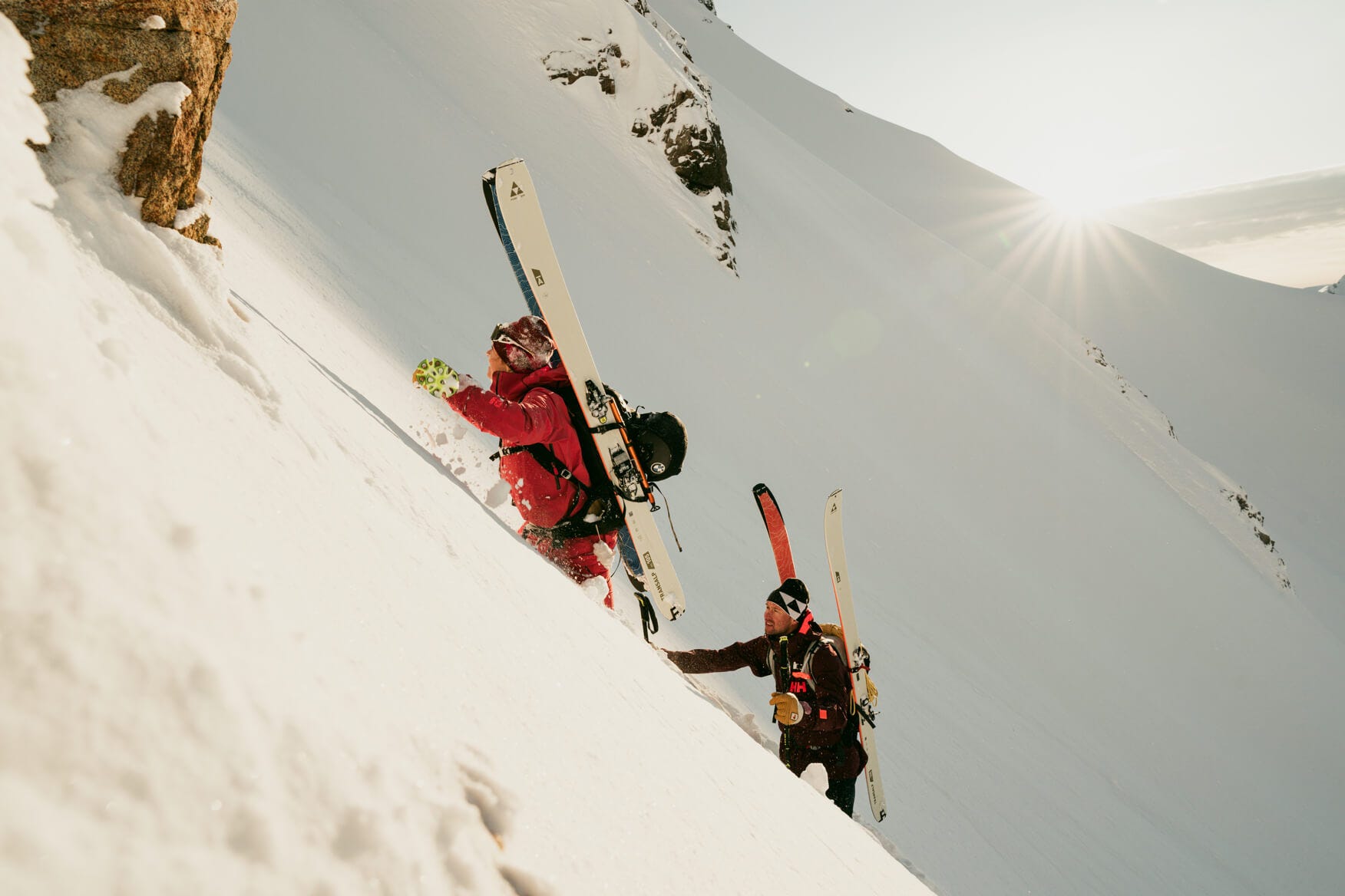 2 people scaling a mountain with skiis on their back in deep powder snow 