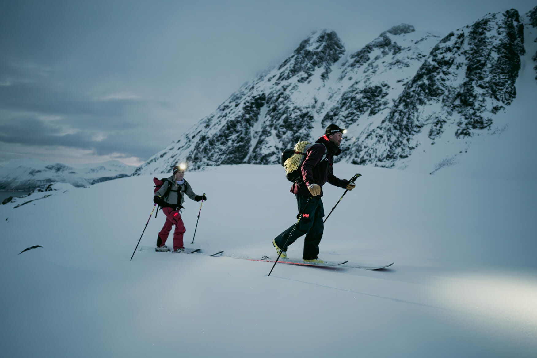 2 people ski touring in the evening with headlamps on 