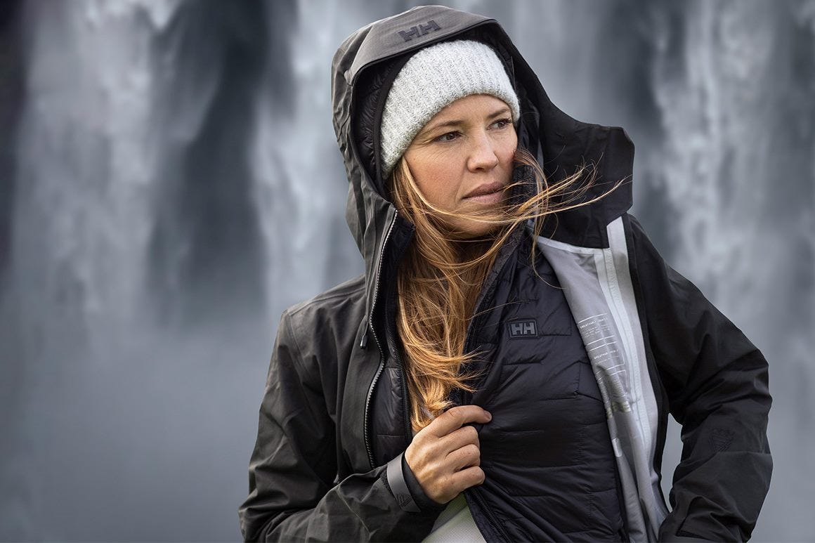 A woman standing by a waterfall wearing a LIFALOFT midlayer underneath a shell jacket