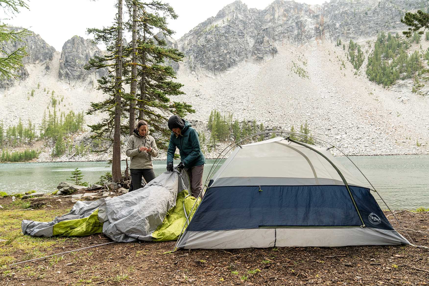 2 people setting up a tent by a lake