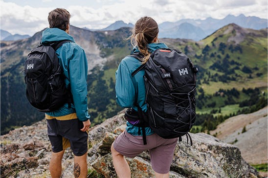 2 hikers with backpacks on, admiring the view from the mountaintop.