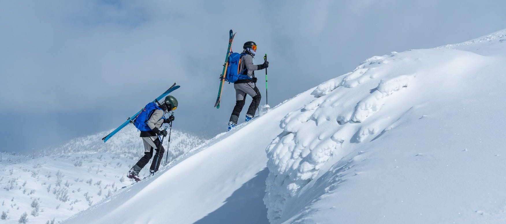 Man and woman ascending a snowy mountain with skis and backpack